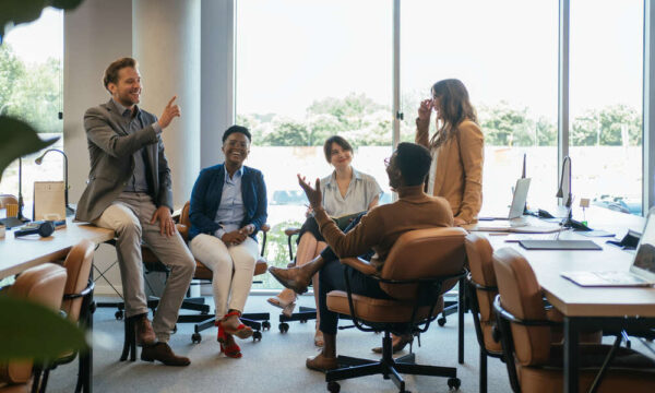 Team of five multi-ethnic employee having fun working together in an open plan office with big windows.