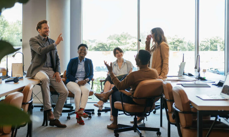 Team of five multi-ethnic employee having fun working together in an open plan office with big windows.