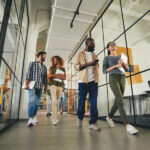 Two couples of joyous young men and women carrying their laptops while walking to the workplace