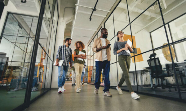 Two couples of joyous young men and women carrying their laptops while walking to the workplace