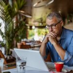 Contemplating businessman in the restaurant feeling sad. Full concentration on work. Confident mature man working on laptop while sitting at his working place in office.