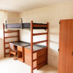An empty university dormitory room with desk bed and closet.