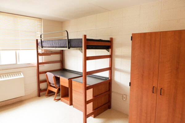 An empty university dormitory room with desk bed and closet.