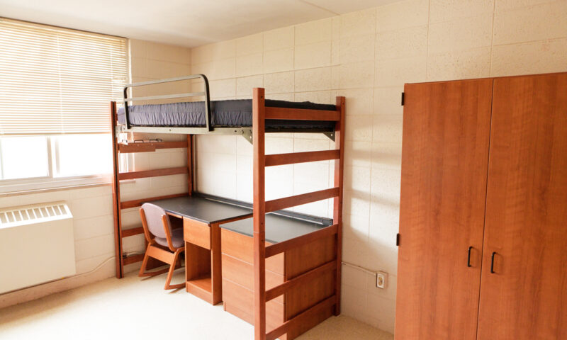 An empty university dormitory room with desk bed and closet.