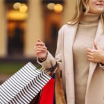 Shopping bags in the hands. Hand of young woman with multi-coloured bags with purchases. Beautiful girl holding shopping bags on the city street. Consumerism, shopping, sales, lifestyle concept.