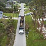 Aerial view of Hurricane Ian special aftermath recovery dump truck picking up vegetation debris from Florida suburban streets. Dealing with consequences of natural disaster.