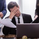 Stressed Businessman Sitting In Office Surrounded By Businesspeople
