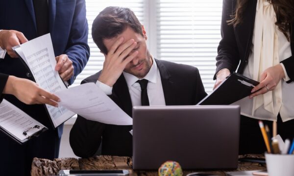 Stressed Businessman Sitting In Office Surrounded By Businesspeople