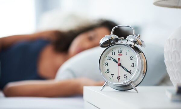 Shot of an attractive young woman laying in bed with an alarm clock on her bedside table