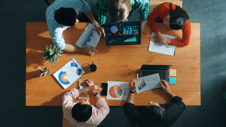 Top down view of business woman explain and present financial chart. Diverse group discuss and listen presentation about stock market statistic at meeting table with investment graph. Convocation.