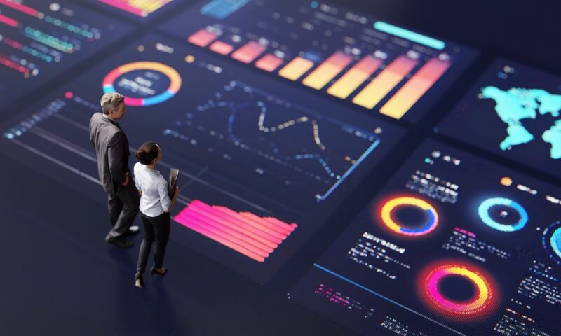 Abstract people standing on a large digital screen, analysing interactive data visualisations and charts for strategic planning. Representing teamwork, technology, and data-driven decision making in a corporate environment.