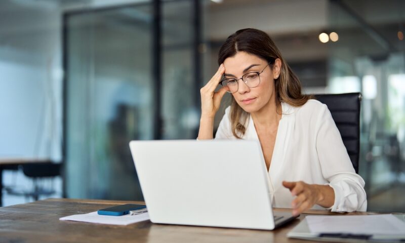 Worried fatigued mature business woman wearing glasses having headache at work. Tired busy 40s middle aged businesswoman feeling stress at workplace looking at laptop computer in office.