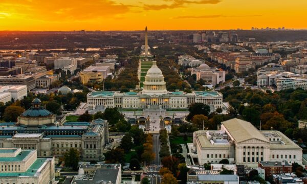 Helicopter shot of the United States Capitol and Supreme Court Building in Washington, D.C. at sunset, with the National Mall in the background.