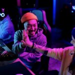 Happy Chinese gamer congratulating his friend on successful video game in entertainment club.