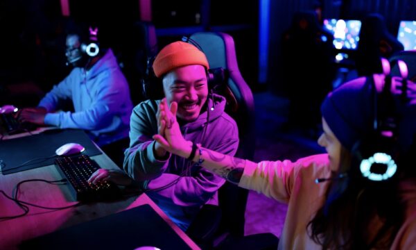 Happy Chinese gamer congratulating his friend on successful video game in entertainment club.