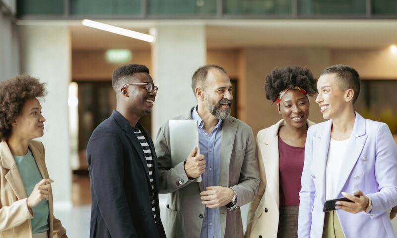 Group of Diverse Coworkers Standing at the Office Corridor and Smiling while Having an Informal Conversation