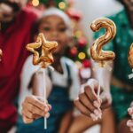 Festive family celebrating the new year at home, holding golden balloons with the numbers 2026. Christmas tree and holiday decorations in the background, joyful and warm atmosphere. Concept of family togetherness, holidays, festive season, new beginnings, 2026 celebration