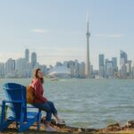 Woman sitting on colourful lounge chairs looking at Toronto cityscape from Toronto island park