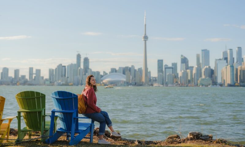 Woman sitting on colourful lounge chairs looking at Toronto cityscape from Toronto island park