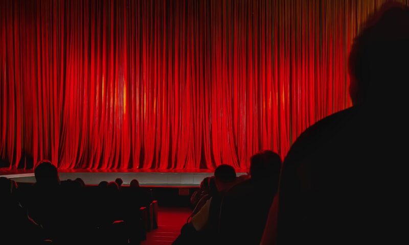 Red Theater Curtain. Closed red theater curtain illuminated by warm stage lights before performance begins. Concept of anticipation, stage performance, entertainment event