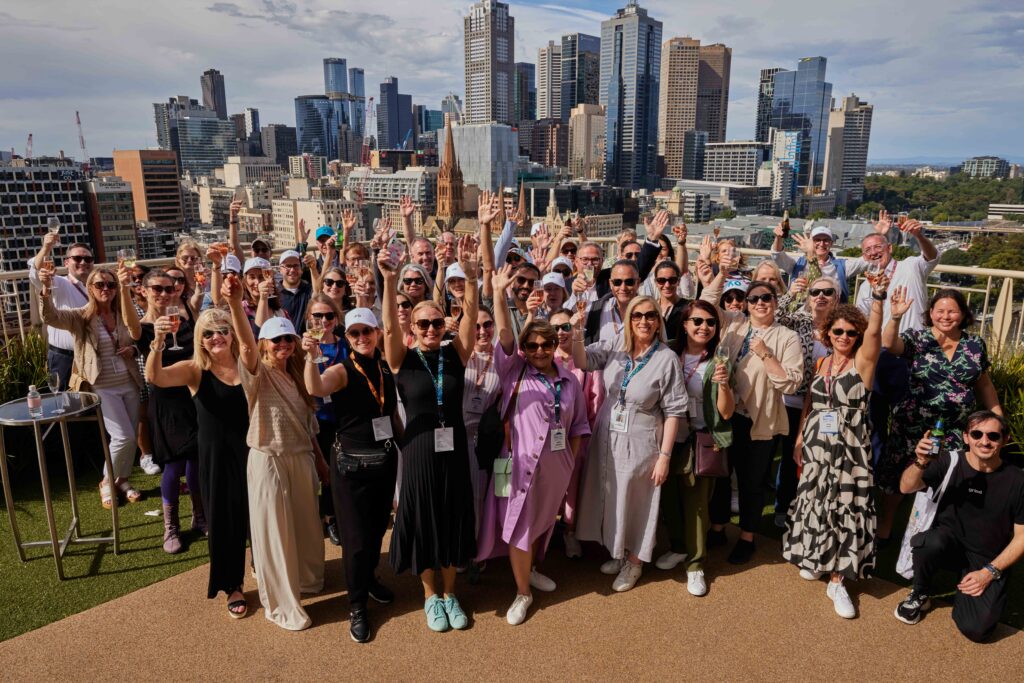 Diverse group at a professional networking event raising their glasses with the Melbourne cityscape in the background.