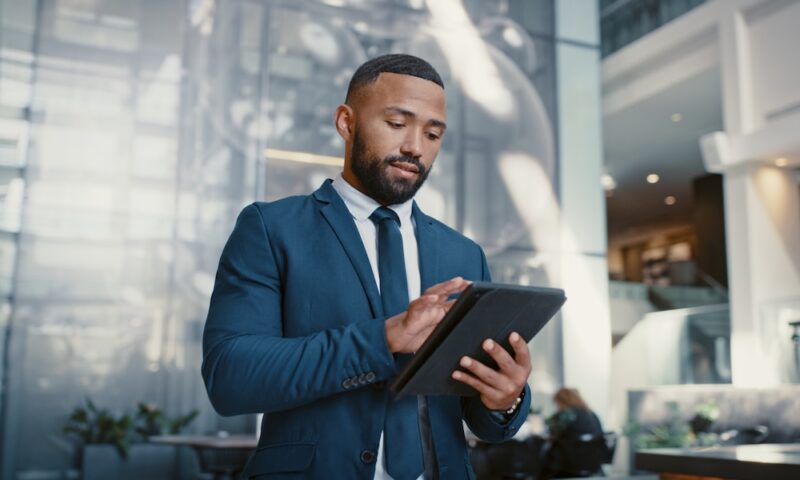Hotel, manager and man on a digital tablet for booking, planning and accommodation management while working at front desk. Black man, concierge and hospitality by male doing online task at reception