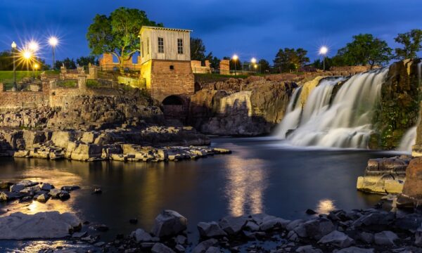 Scenic waterfall and historic mill building illuminated at night at Falls Park in downtown Sioux Falls, South Dakota