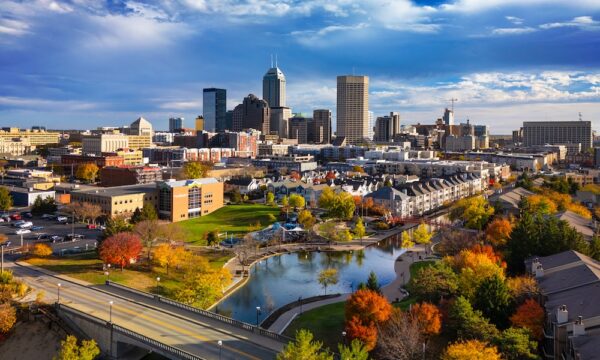 Beautiful aerial view of the Indiana Central Canal in Indianapolis during autumn, with the Downtown Indianapolis skyline in the background and lush colored trees in the foreground.